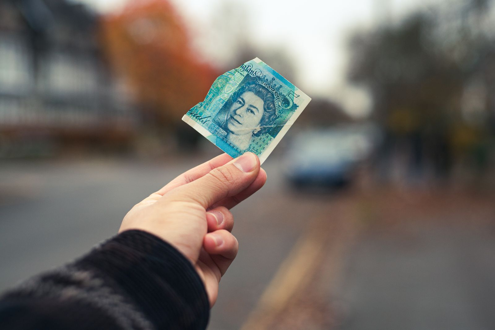 A hand holding out a five pound note on a quiet residential street