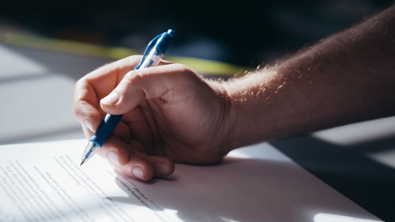 A hand signing a printed document with a pen