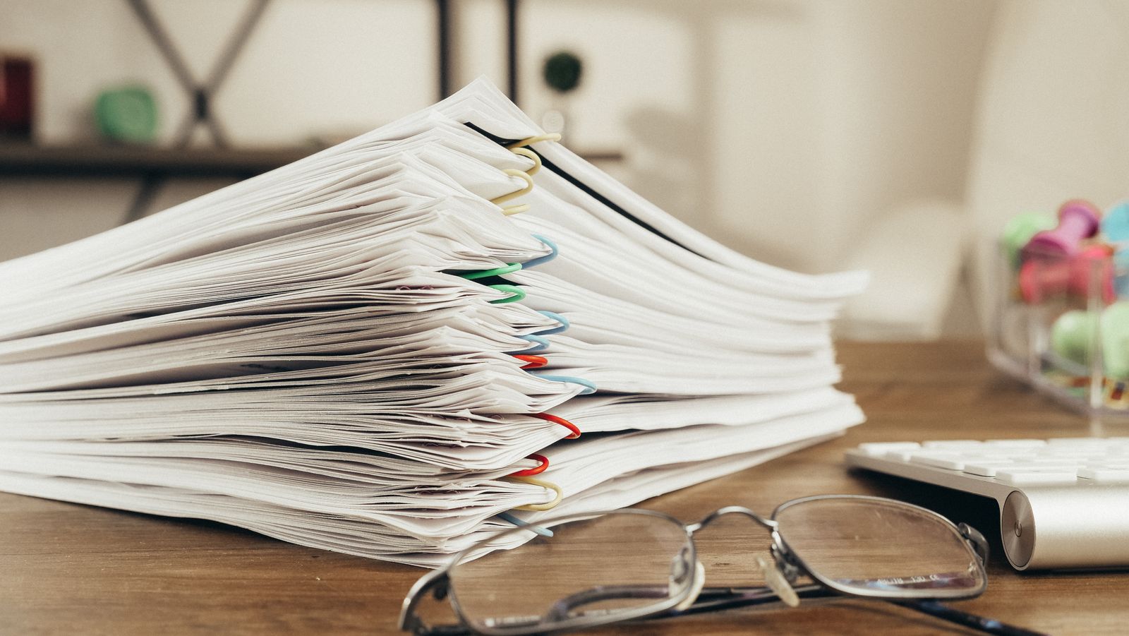 A thick stack of clipped paper documents beside a pair of glasses